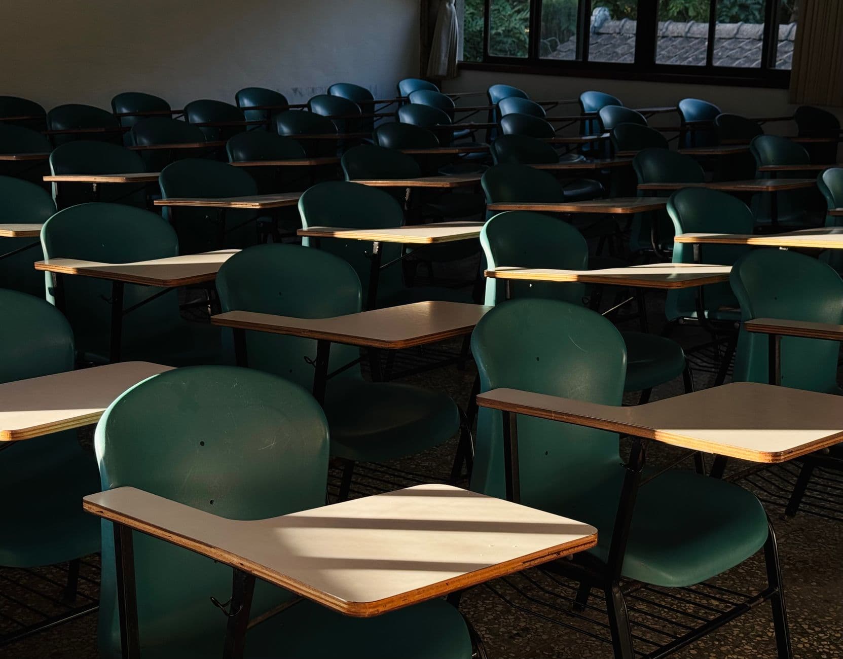Ruang kelas kosong dengan meja belajar yang diterpa cahaya matahari dari jendela